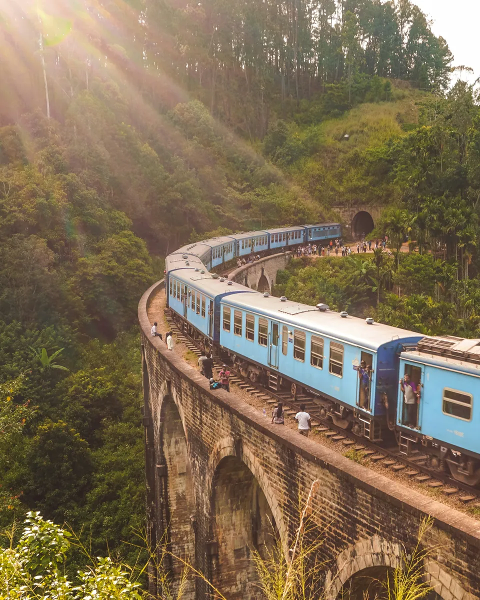 Blue train crossing a stone viaduct through Sri Lanka's green hill country