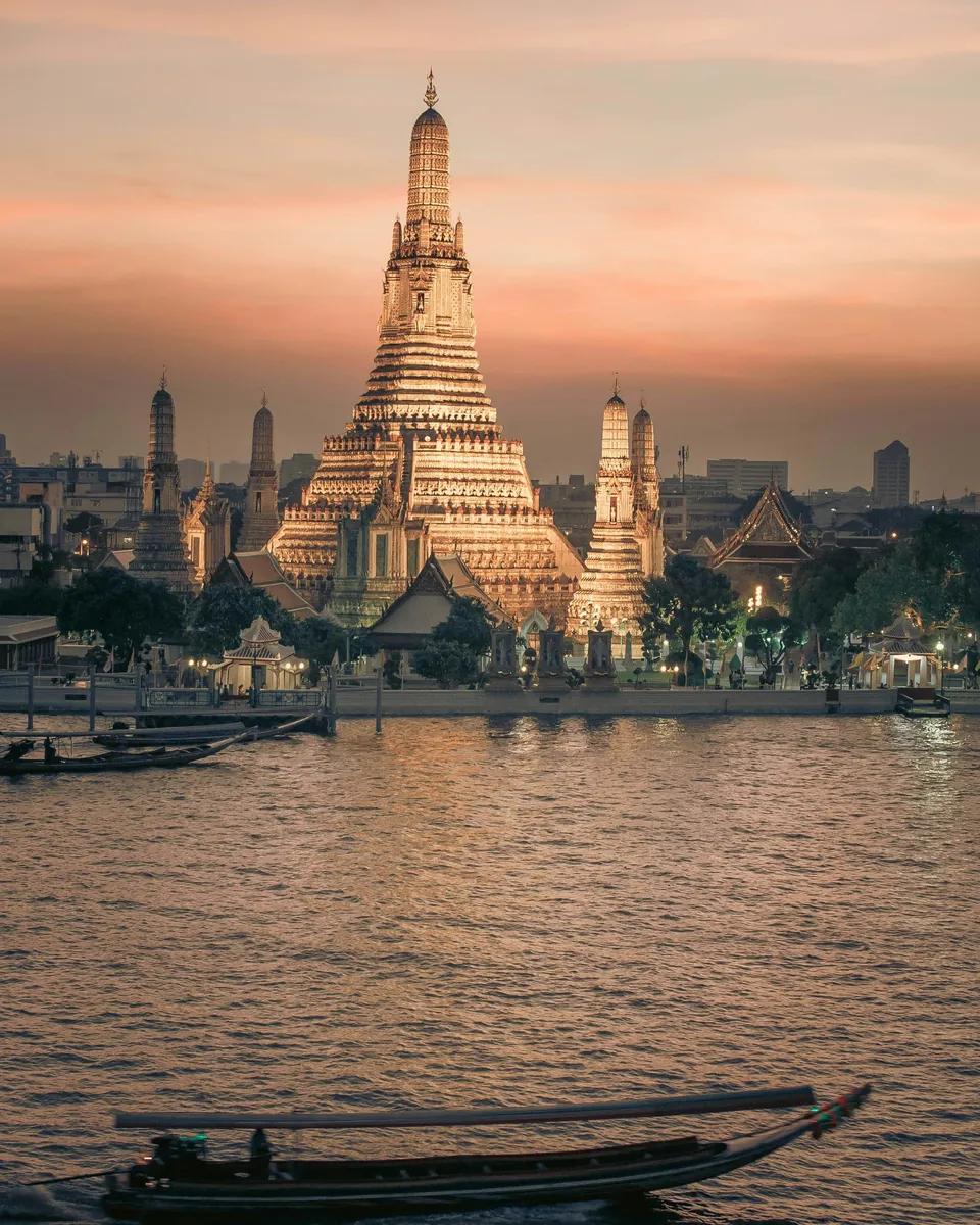 Wat Arun temple on Bangkok's river at sunset, with a longtail boat in the foreground